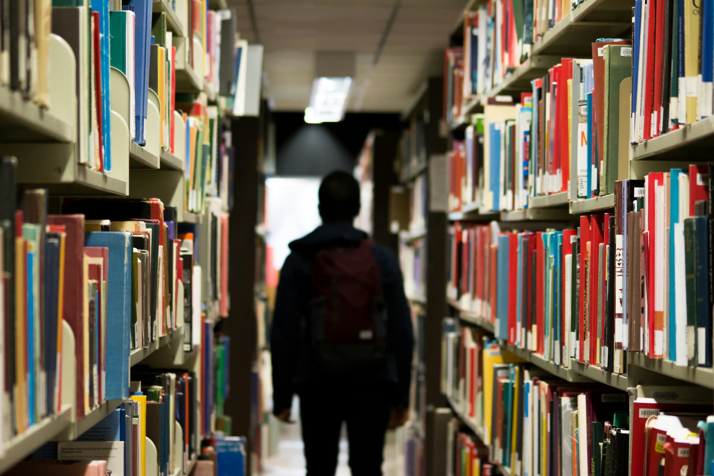 Student walking between tall library bookshelves