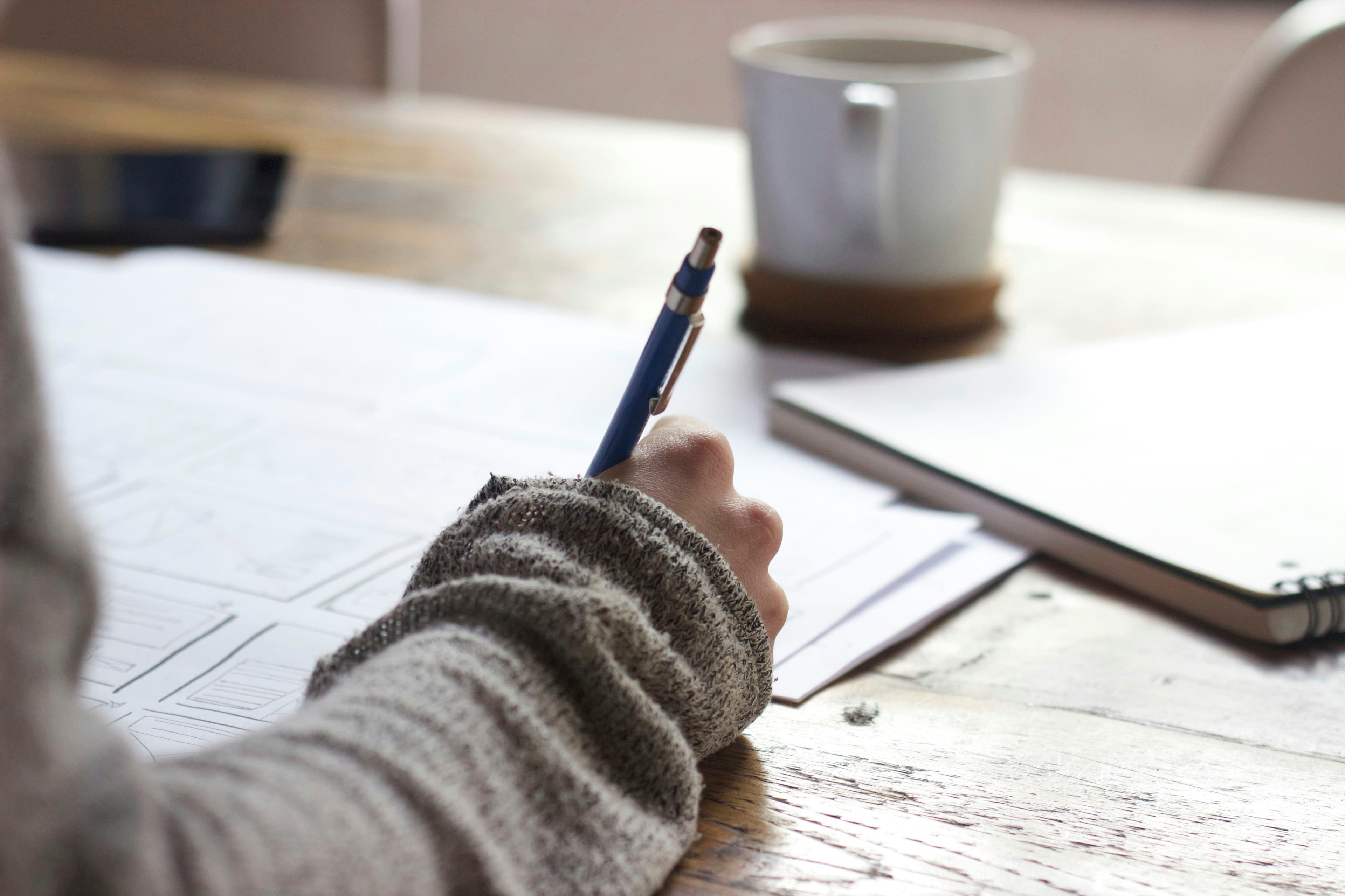 Student writing notes at a desk with a cup of coffee