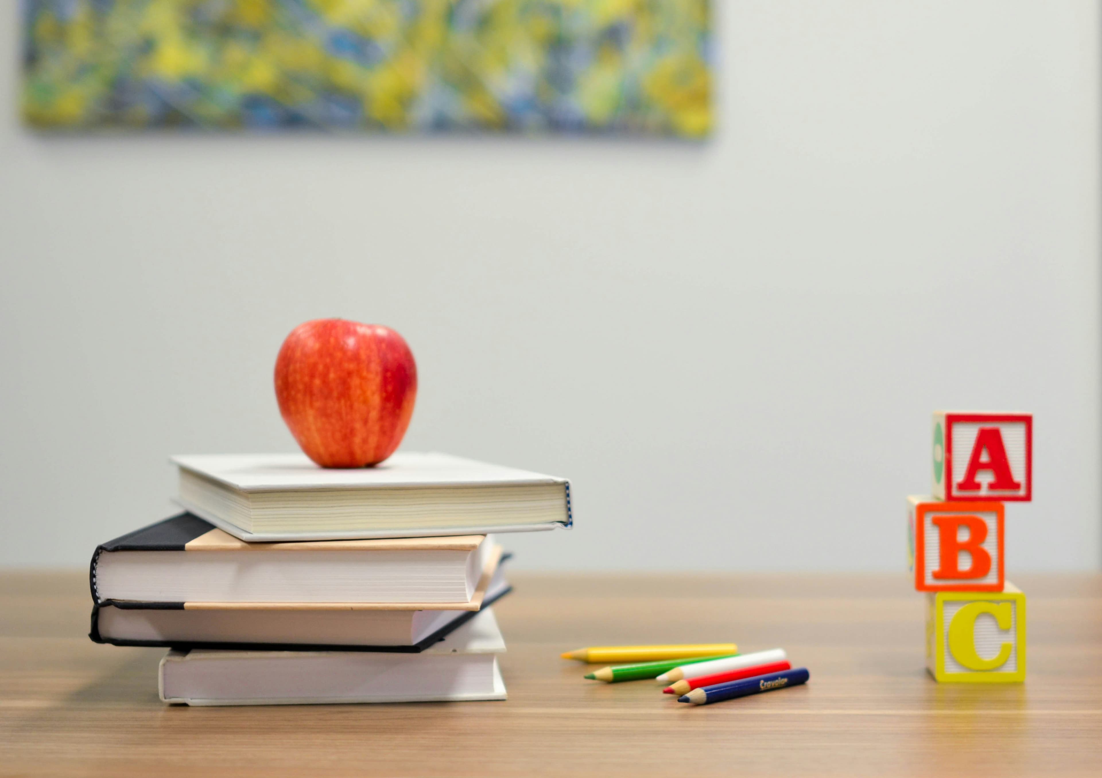 Stack of books with an apple and alphabet blocks on a desk